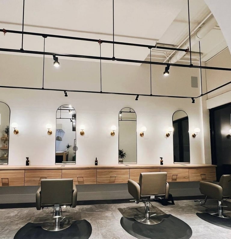 Modern hair salon interior with salon chairs, large mirrors, track lighting, and wood paneling below white walls