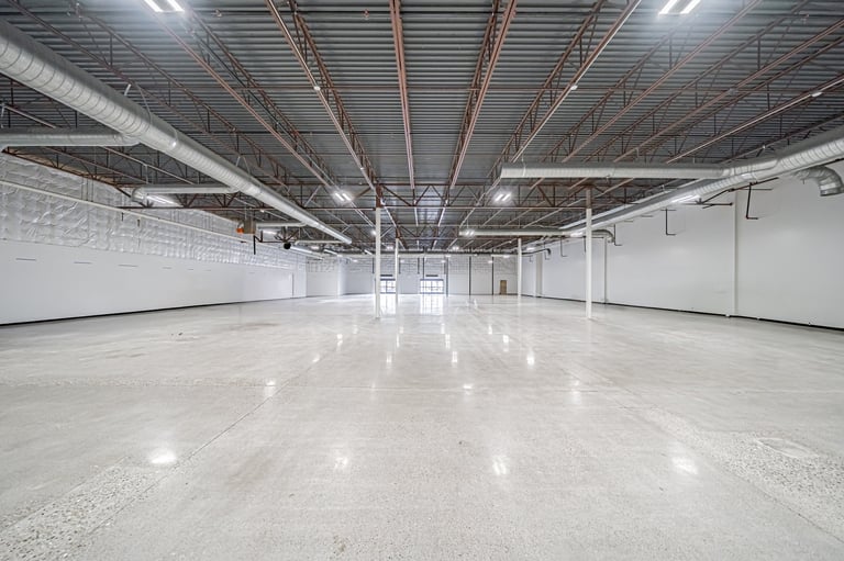 Empty industrial warehouse interior with polished concrete floor, metal ceiling beams, and fluorescent lighting