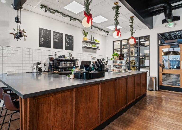 Modern cafe interior with wooden counter, espresso machine, and holiday decorations hanging from ceiling