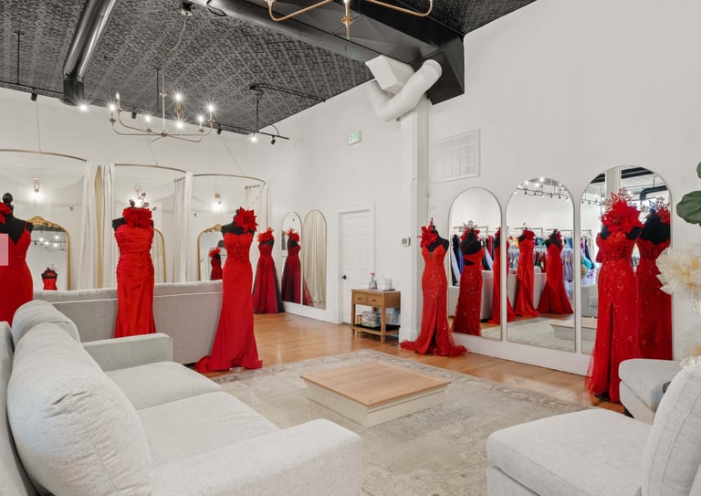 Modern boutique interior with red evening gowns displayed on mannequins and mirrors, white seating, and polished wood flooring