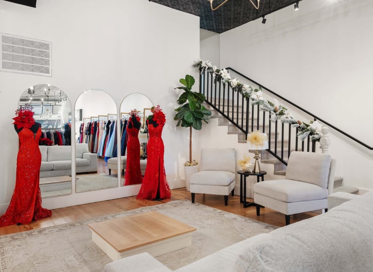 Modern boutique showroom with red dresses on display, seating area, mirror, and staircase decorated with garland