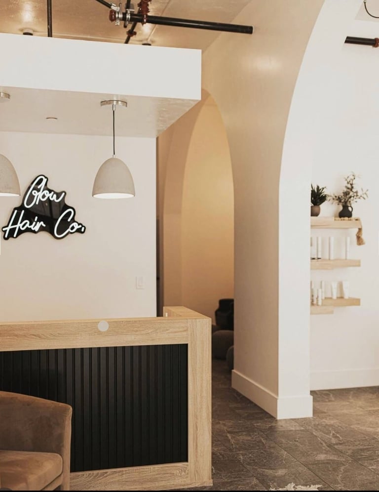 Modern hair salon interior with wooden reception desk, neon Boa Hair Co sign, pendant lighting, and cream-colored walls
